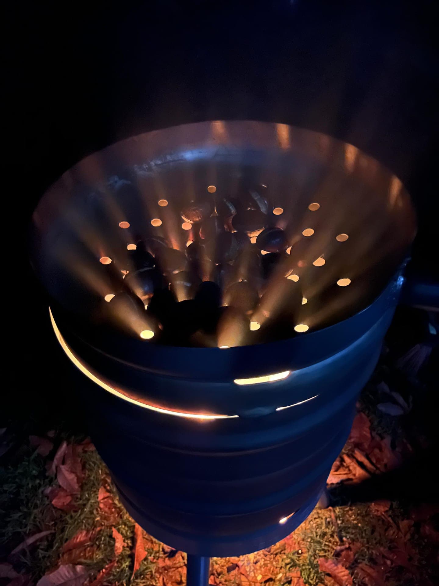 Blaue Maronen-Rösttonne mit warmem Feuerlicht am Abend auf Laub